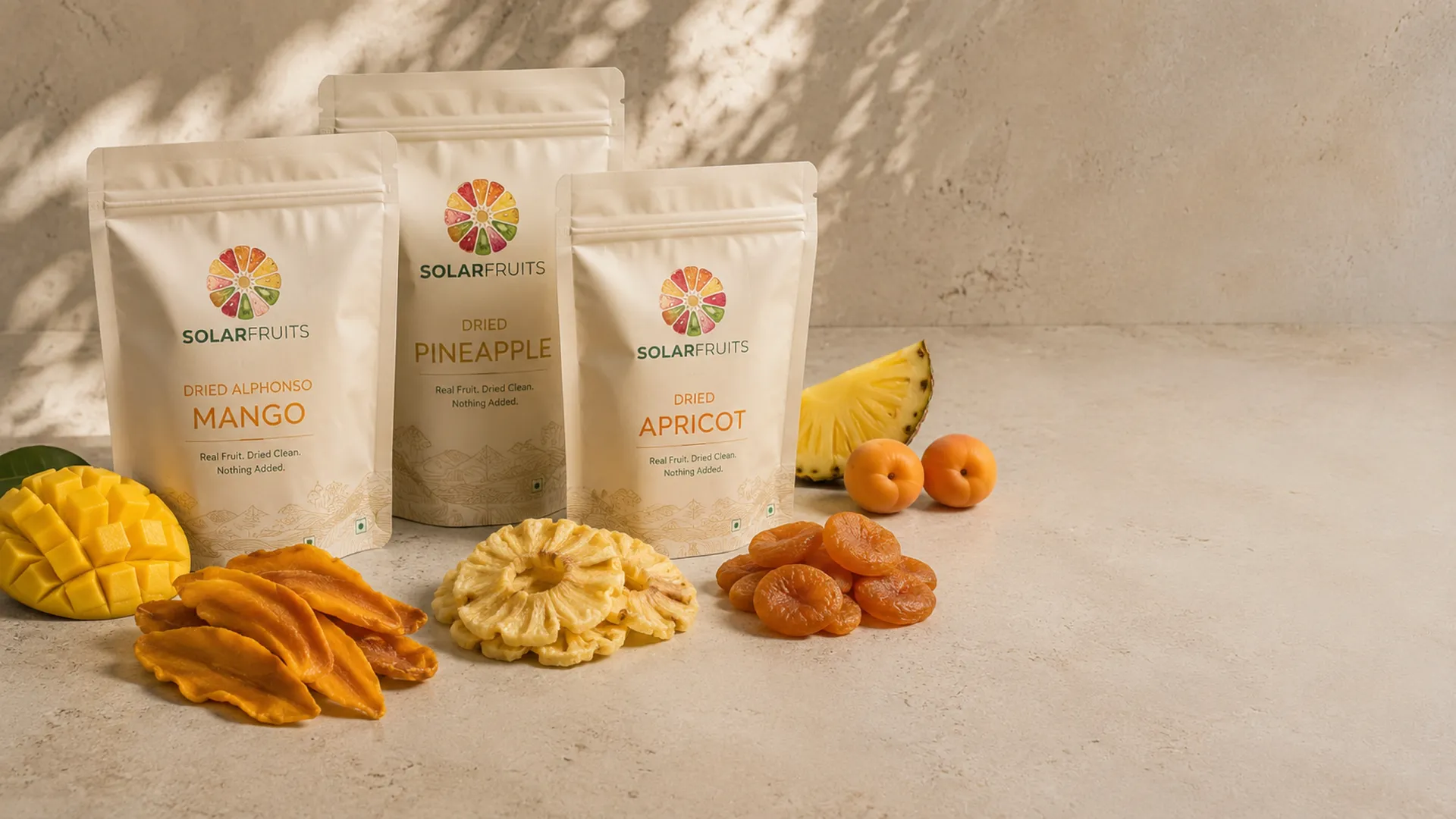 Solar Fruits packs of sun-dried mango, pineapple and apricot, with fresh and dried fruit on a warm surface